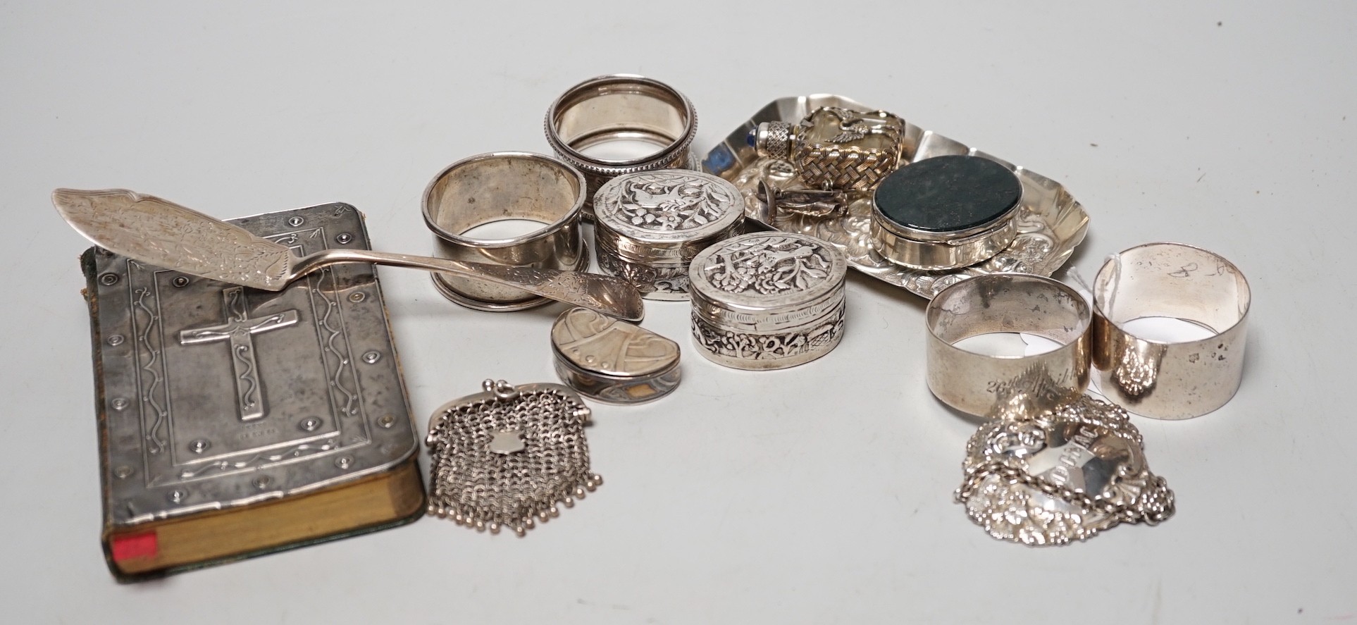 Sundry small silver including four assorted napkin rings, mounted bible, butter knife, pin tray, wine label etc. together with two white metal oval pill boxes, a moss agate mounted oval pill box and scent bottle.